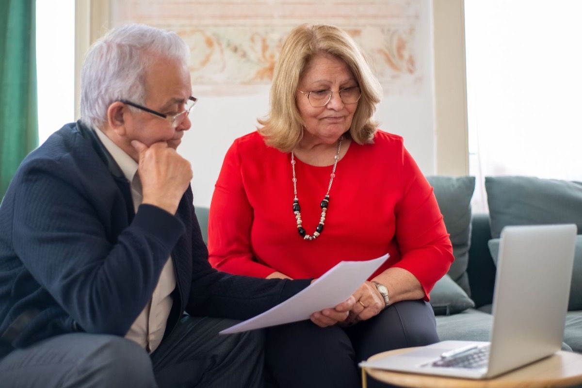 A couple in their 60s reviewing financial documents together on a sofa at home