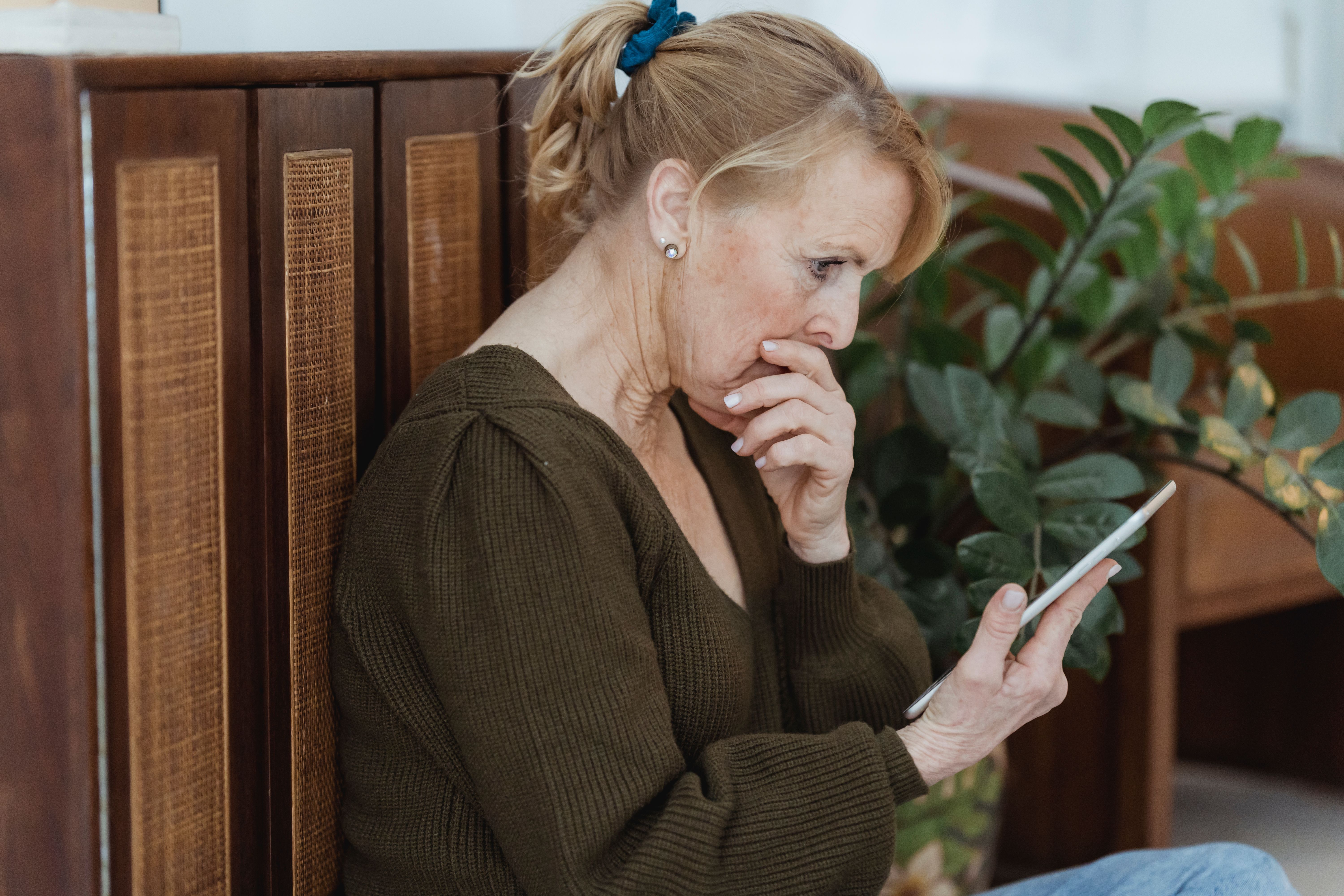 Woman over 50 looking at her phone with concern, hand near her mouth, processing a troubling message