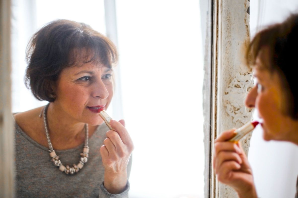 Mature woman applying lipstick while smiling at her reflection